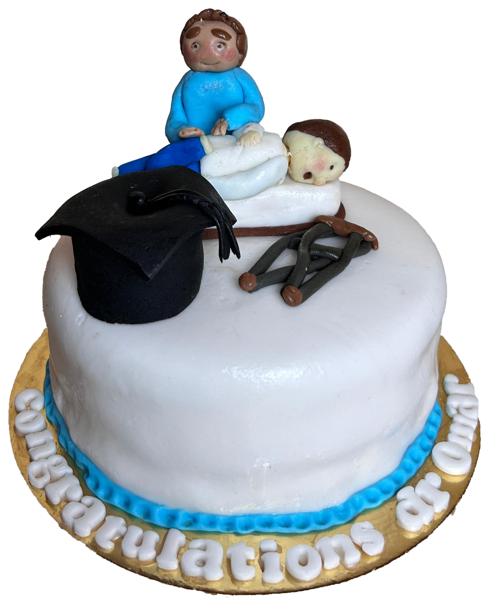 A white graduation cake with a sugar graduation cap and figures on top, and "Congratulations" in sugar letters around the board